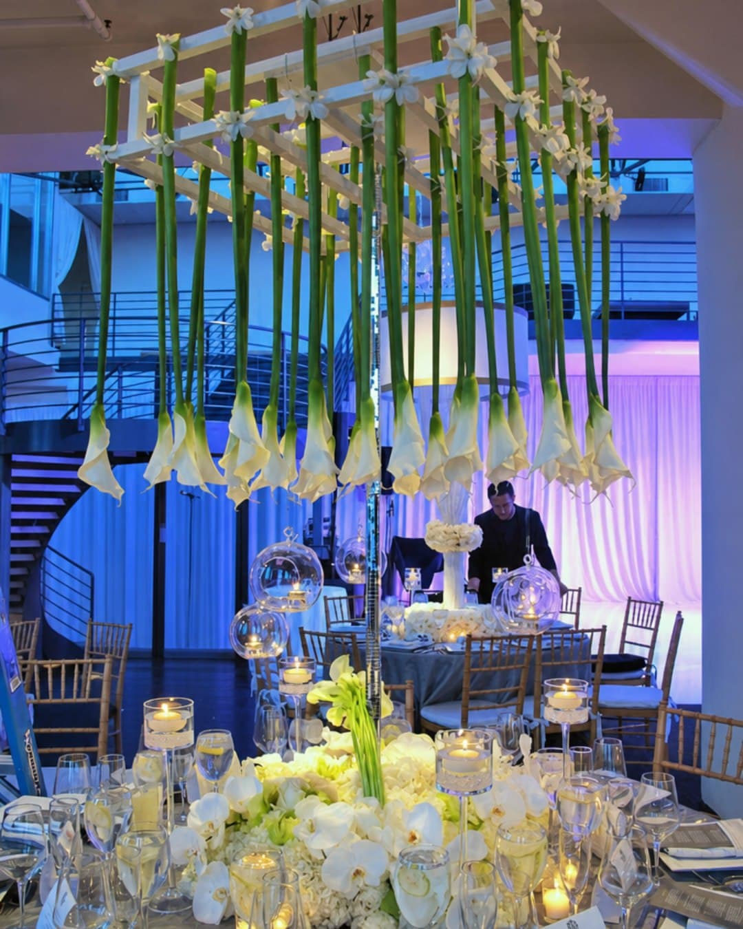 Centro floral colgante de calas blancas sobre la mesa de un banquete de boda
